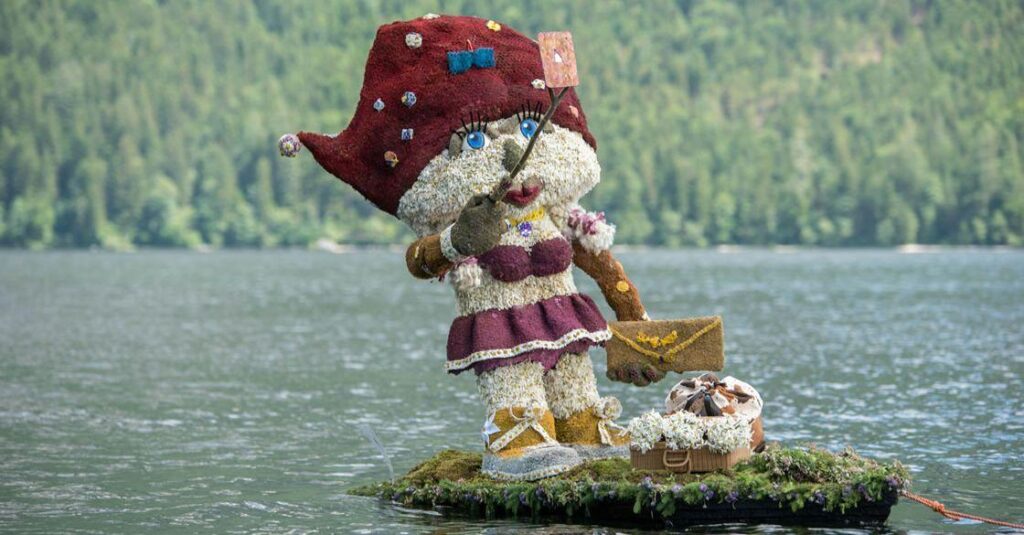 Figur aus Narzissenblüten beim Narzissenfest im Salzkammergut, aufgenommen am Wasser mit Bergen im Hintergrund.