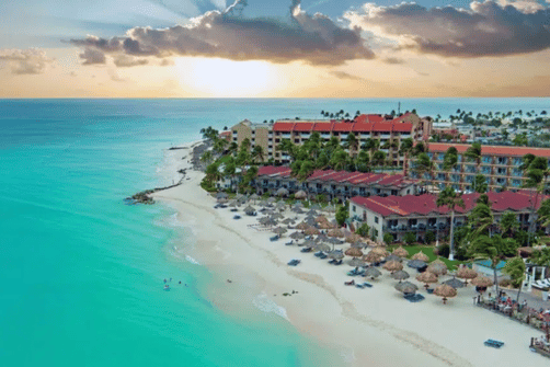 beste Reisezeit Karibik – Strandresort mit Palmen und türkisblauem Meer bei Sonnenuntergang