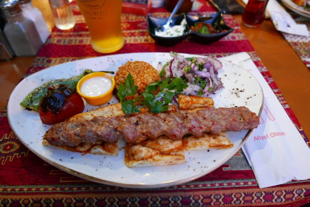 Turecki Adana kebab podany z ryżem, grillowanymi warzywami i dodatkami.